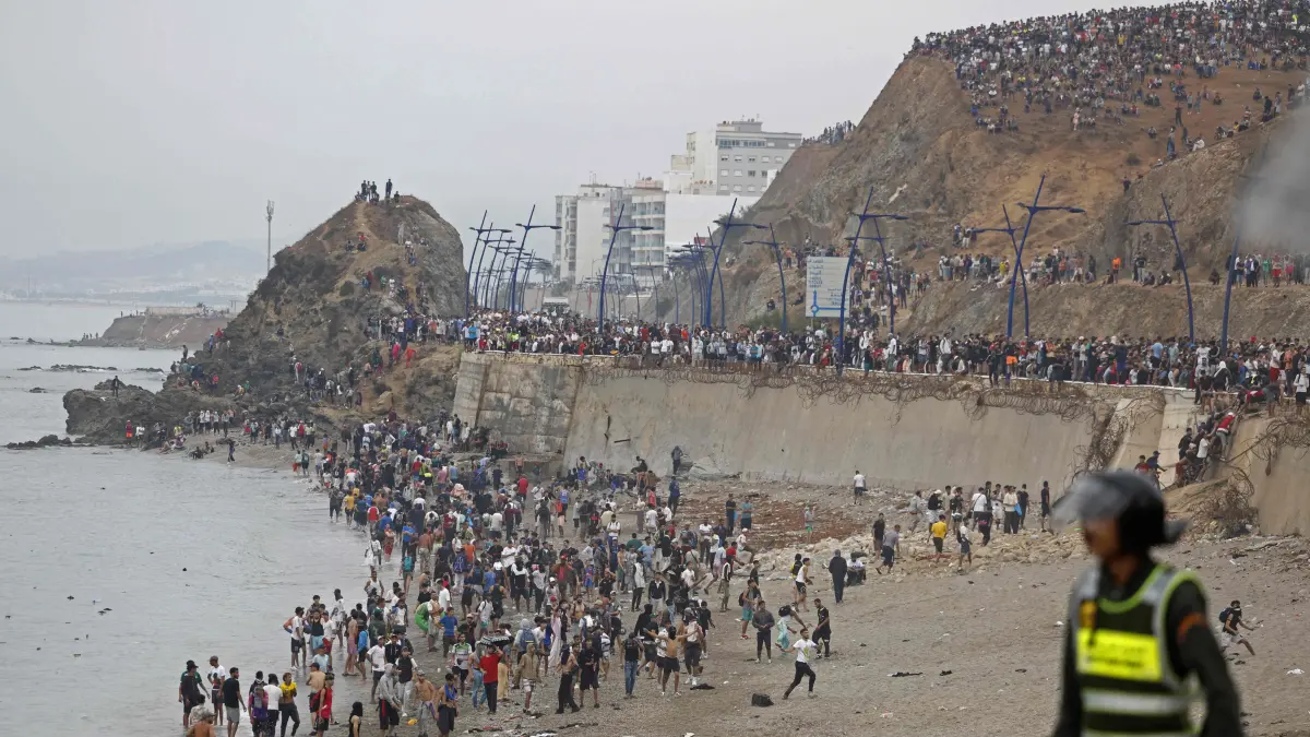 MOROCCO-SPAIN-MIGRATION: People gather along the fence at the site of clashes near Fnideq, on the Morocco-Spain border, on July 31, 2026. Thousands of migrants crossed overnight from Morocco into Spain's north Africa's Ceuta enclave, a police source said on July 31, as Prime Minister Pedro Sanchez was set to arrive to manage the latest migrant crisis on the border. (Photo by Abdel Majid BZIOUAT / AFP)