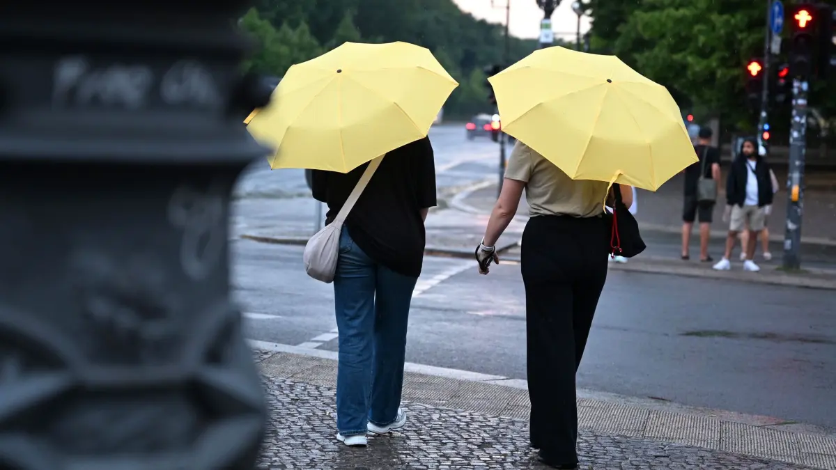 Wetter in Berlin und Brandenburg: ARCHIV - 17.07.2026, Berlin: Zwei Frauen laufen mit Regenschirm vor dem Brandenburger Tor während Regen über Berlin zieht. (zu dpa: «Sonne folgt auf Unwetter») Foto: Elisa Schu/dpa +++ dpa-Bildfunk +++