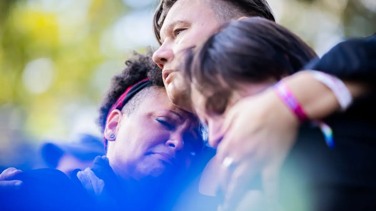 Mahnwache nach dem Angriff auf CSD in Berlin: 02.08.2026, Berlin: Mo (l-r), Katja und Isabelle trauern bei einer Mahnwache für die Opfer des Anschlags auf den CSD im Tiergarten. Dort war am Rande des Christopher Street Day ein Mann mit einem Fahrzeug in eine Menschenmenge gefahren. Foto: Christoph Soeder/dpa - ACHTUNG: Nur zur redaktionellen Verwendung im Zusammenhang mit der aktuellen Berichterstattung und nur mit vollständiger Nennung des vorstehenden Credits +++ dpa-Bildfunk +++