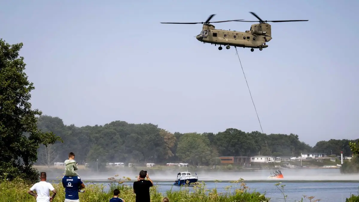Tagesausflügler beobachten, wie ein Wassersack unter einem Chinook-Hubschrauber in der Maas befüllt wird. Mehrere Löschhubschrauber der Luftwaffe sind im Einsatz, um einen Waldbrand im Naturschutzgebiet Boschhuizerbergen zu bekämpfen. Rund 100 Hektar sind von dem Feuer betroffen.