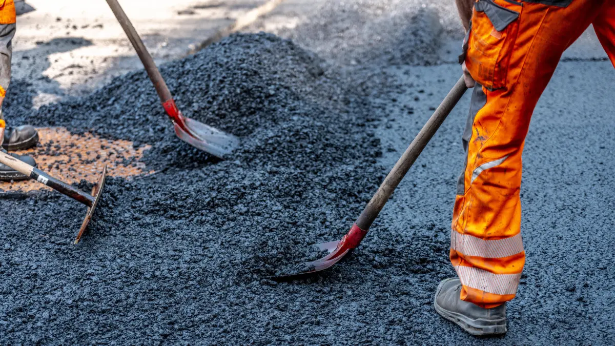 Straßenbau, Straßenbauarbeiten, Arbeiter bessern einen Teil einer innerstädtischen Straße mit Asphalt aus, der heiße Asphalt wird von Hand um einen Kanaldeckel verteilt, anschließend mit einer Straßenwalze verdichtet und geplättet, NRW, Deutschland, Straßenbau *** Road construction, road construction work, workers repair part of an inner-city road with asphalt, the hot asphalt is spread by hand around a manhole cover, then compacted and flattened with a road roller, NRW, Germany, road construction