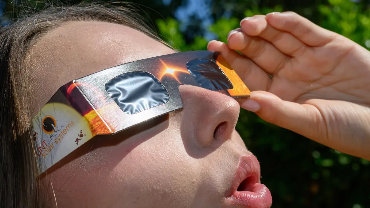 Vorfreude auf die Sonnenfinsternis: 09.08.2026, Brandenburg, Sieversdorf: Eine junge Frau schaut durch eine Sonnenfinsternisbrille und betrachtet die Mittagssonne über Brandenburg. Das Zentralgestirn steht derzeit im Fokus der Astronomie, da am Abend des 12.08.2026 eine bedeutende partielle Sonnenfinsternis stattfindet. Foto: Patrick Pleul/dpa +++ dpa-Bildfunk +++
