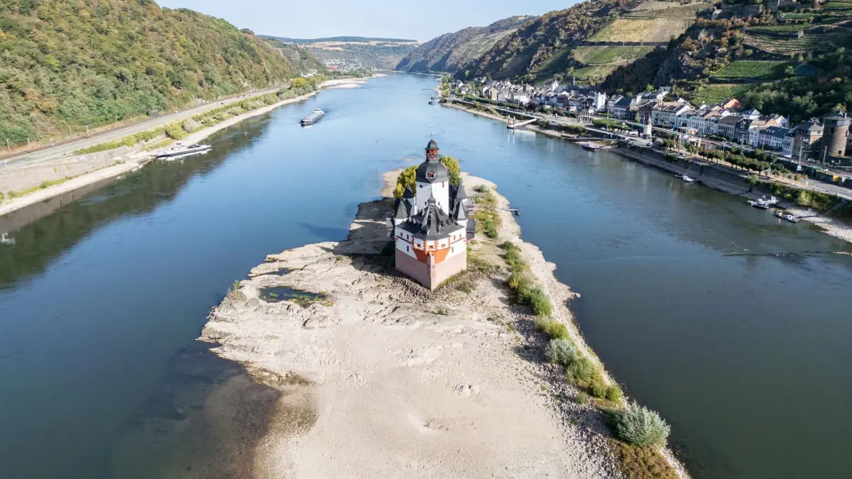 Extremes Niedrigwasser auf dem Rhein: 09.08.2026, Rheinland-Pfalz, Kaub: Extremes Niedrigwasser auf dem Rhein lässt an der Festung Pfalzgrafenstein den Grund des Flusses sichtbar werden (Luftaufnahme mit einer Drohne). Die Binnenschifffahrt ist bereits massiv eingeschränkt und droht gänzlich zum Erliegen zu kommen. Foto: Boris Roessler/dpa +++ dpa-Bildfunk +++