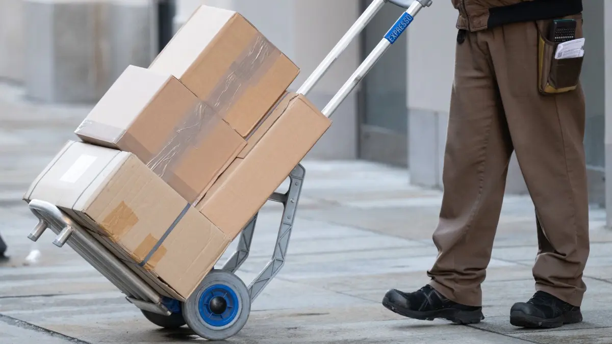 Paketzusteller: ARCHIV - 01.12.2025, Sachsen, Dresden: Ein Paketzusteller von UPS steht mit einer Transportkarre mit mehreren Paketen auf dem Fußweg. (zu dpa: «Neue EU-Verpackungsregeln sorgen für Unmut») Foto: Sebastian Kahnert/dpa +++ dpa-Bildfunk +++