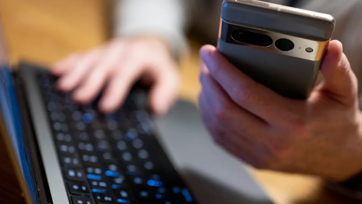 Online-Banking: ILLUSTRATION - 27.02.2023, Berlin: Ein Mann sitzt am Laptop und hält ein Smartphone mit in der Hand. Der Digitalverband Bitkom sieht einen ungebrochenen Trend zum Online-Banking. (zu dpa: «Millionenbetrug an Bankkunden: Ermittler heben Netzwerk aus») Foto: Monika Skolimowska/dpa +++ dpa-Bildfunk +++