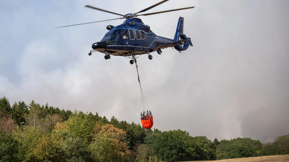 Waldbrand im Hürtgenwald: 14.08.2026, Nordrhein-Westfalen, Hürtgenwald: Ein Helikopter der Bundespolizei mit einem Löschwasser-Außenlastbehälter ist beim Waldbrand im Hürtgenwald im Einsatz. Mehrere Hundert Hektar Waldfläche stehen in Flammen. (zu dpa: «Mehrere Löschhubschrauber bei Hürtgenwald erwartet») Foto: Harald Tittel/dpa +++ dpa-Bildfunk +++