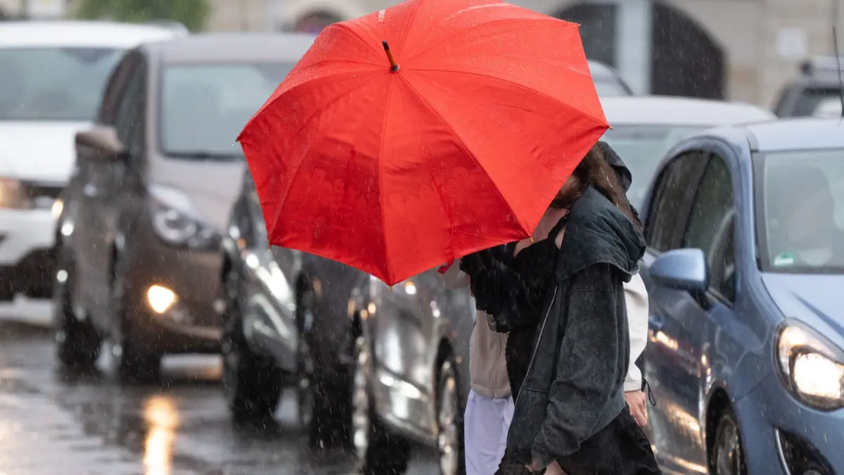 Wetter in Sachsen: ARCHIV - 21.07.2025, Sachsen, Bautzen: Passanten überqueren bei Starkregen mit einem Regenschirm eine Straße. Der Deutsche Wetterdienst (DWD) hat für Sachsen kühlere Temperaturen und Regen vorausgesagt. (zu dpa: «Gewitter und Regen zum Start in die neue Woche») Foto: Sebastian Kahnert/dpa +++ dpa-Bildfunk +++