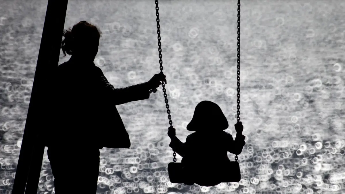 Mutter mit Kind: ARCHIV - 16.09.2013, Hamburg: Eine Mutter schaukelt ihr Kind auf einem kleinen Spielplatz am glitzernden Wasser der Alster. (zu dpa: «SPD lehnt Prien-Pläne für Unterhaltsvorschuss ab») Foto: Christian Charisius/dpa +++ dpa-Bildfunk +++