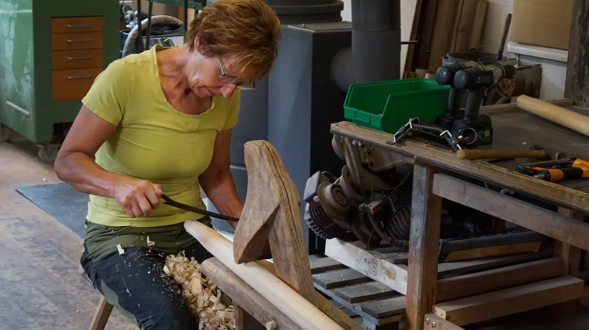 Szene aus dem Film "Wie man eine Obstleiter baut": Ingrid Ertel sitzt auf dem Schneidstuhl ihres Großvaters und hobelt mit dem Ziehmesser Späne von der späteren Stütze für die Obstleiter.