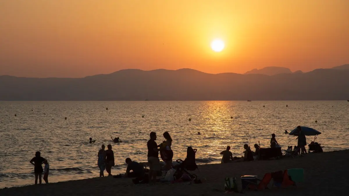 Am Strand von Playa de Palma auf Mallorca baden Menschen bei Sonnenuntergang im Meer. Die hohen Temperaturen locken viele Einheimische und Besucher an, sich bei Sonnenuntergang und in der Nacht am Meer zu erfrischen.