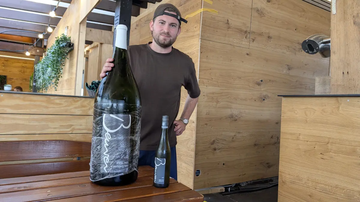 Winzer Adrian Beurer mit der 15-Liter-Weinflasche in der Winzerlaube am Weinbrunnen, die er gemeinsam Mit Johannes Bauerle betreibt.