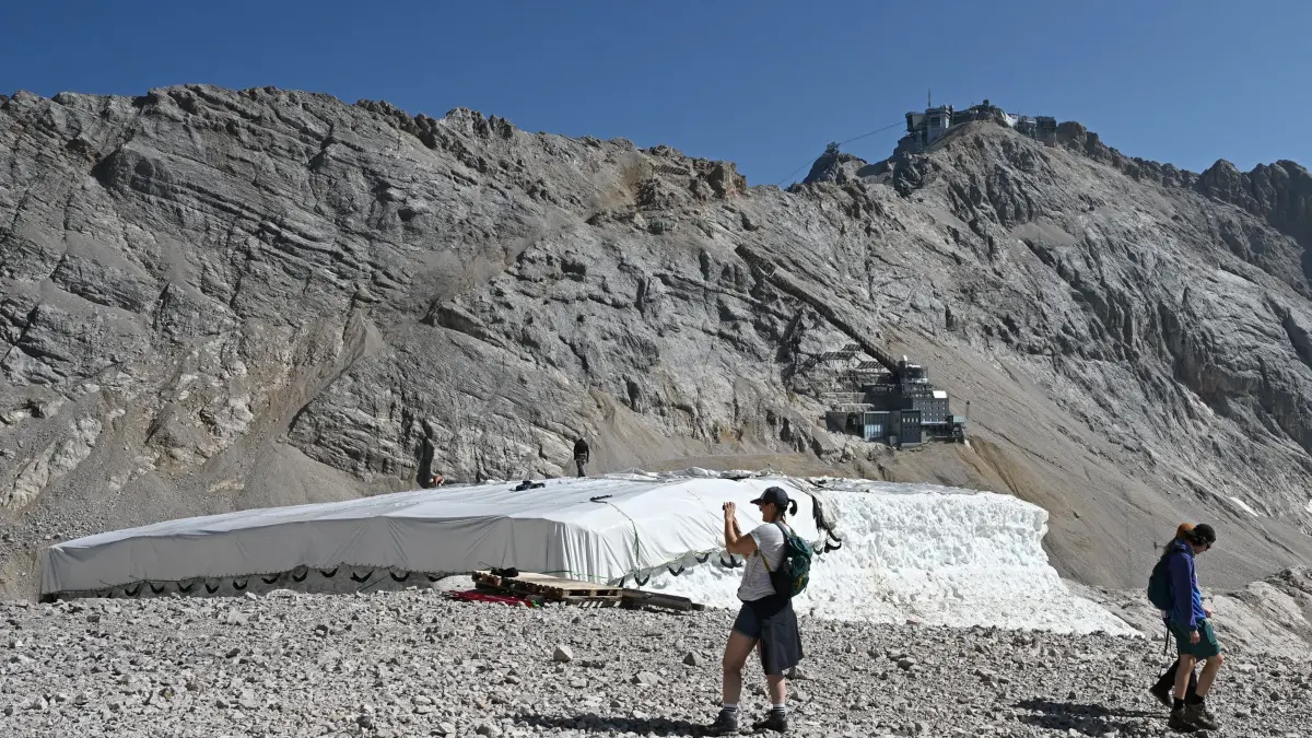 Hitze lässt Gletscher schrumpfen: ARCHIV - 04.08.2026, Bayern, Grainau: Eine Person macht Fotos neben Abdeckfolien auf einem Schneedepot neben den Überresten des Nördlichen Schneeferner-Gletschers auf der Zugspitze. (zu dpa: «Deutschlands letzte Gletscher: Abschied vom ewigen Eis») Foto: Angelika Warmuth/dpa - ACHTUNG: Verwendung nur im vollen Format +++ dpa-Bildfunk +++