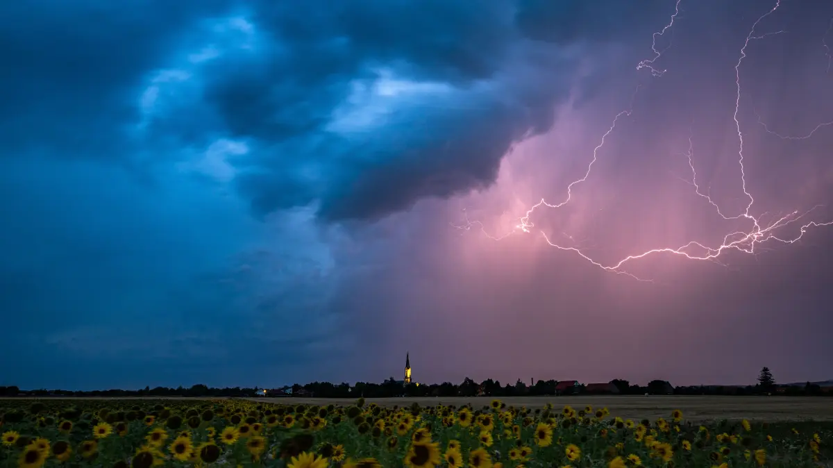 Blitze zucken am Abend über Wechmar mit der Dorfkirche Sankt Viti (Mi.) während Gewitter über Teile von Thüringen ziehen (Archivfoto).