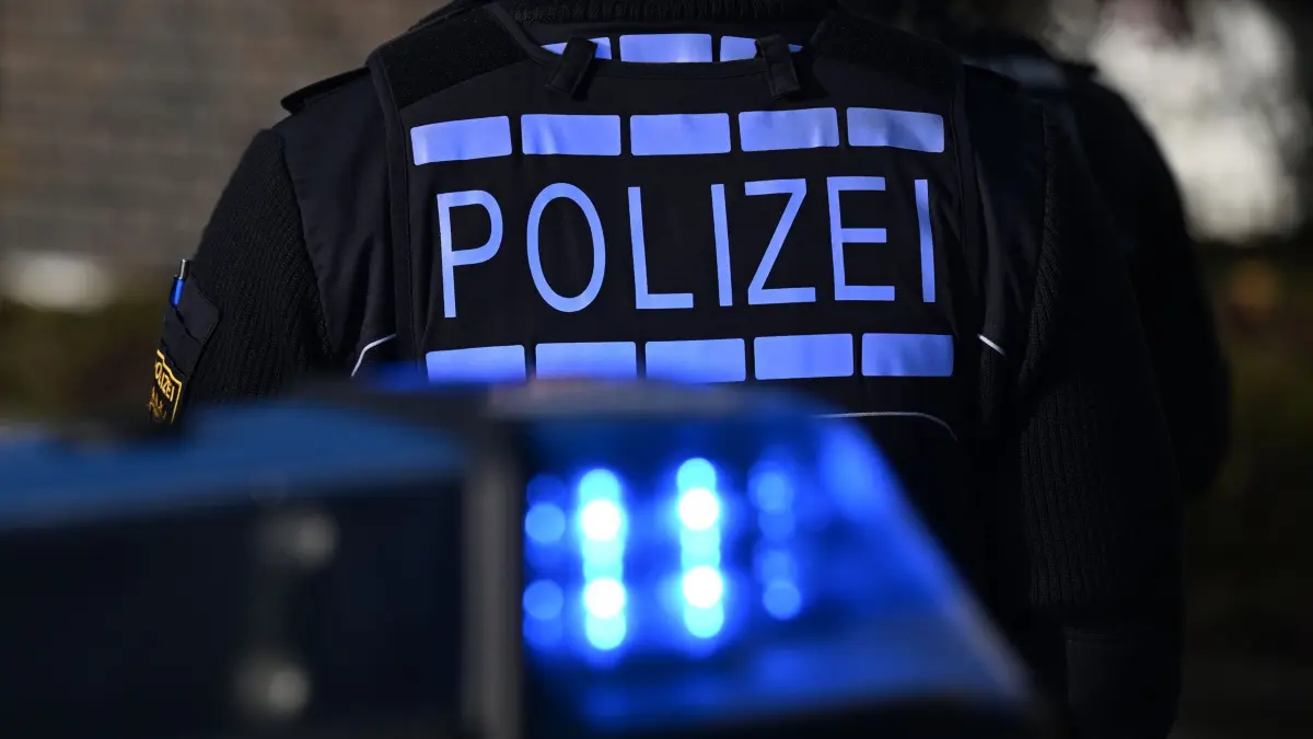 Polizei: ARCHIV - 03.12.2024, Baden-Württemberg, Stuttgart: Das Logo der Polizei auf der Dienstkleidung eines Polizisten der vor einem Blaulicht steht (gestellte Szene). (zu dpa: «Junger Mann rast mit Tempo 130 durch Innenstadt») Foto: Bernd Weißbrod/dpa +++ dpa-Bildfunk +++