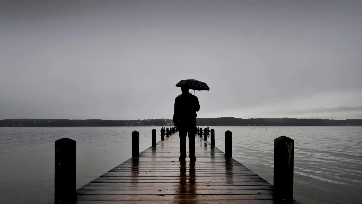Ein Mann steht mit einem Regenschirm auf einem Steg