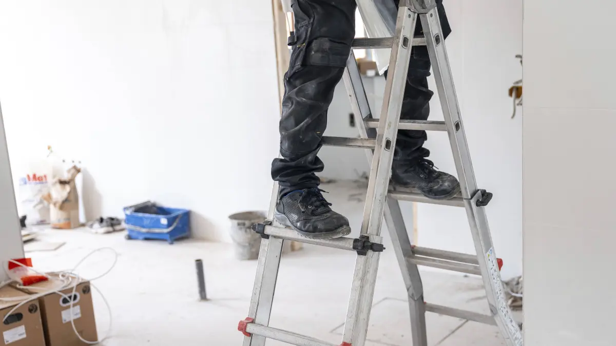Arbeiter, der vorsichtig auf einer tragbaren Aluminiumleiter steht, Sicherheitsschuhe und hosen trägt und Renovierungsarbeiten in einem im Bau befindlichen Wohn oder Geschäftshaus durchführt Worker carefully standing on a portable aluminum ladder, wearing safety work boots and pants, performing renovation tasks in a residential or commercial building under construction Copyright: imageBROKER/UnaixHuizi ibluhu16952662.jpg ,model released, Symbolfoto ,property released Bitte beachten Sie die gesetzlichen Bestimmungen des deutschen Urheberrechtes hinsichtlich der Namensnennung des Fotografen im direkten Umfeld der Veröffentlichung