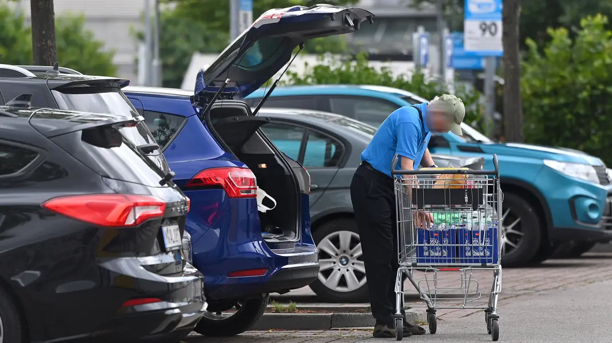 Mann mit Einkaufswagen auf einem Supermarkt Parkplatz. Nach seinem Einkauf belaedt ein aelterer Mann seinen PKW bei geoeffnezer Heckklappe. *** A man with a shopping cart in a supermarket parking lot. After finishing his shopping, an elderly man is loading his car with the trunk open.