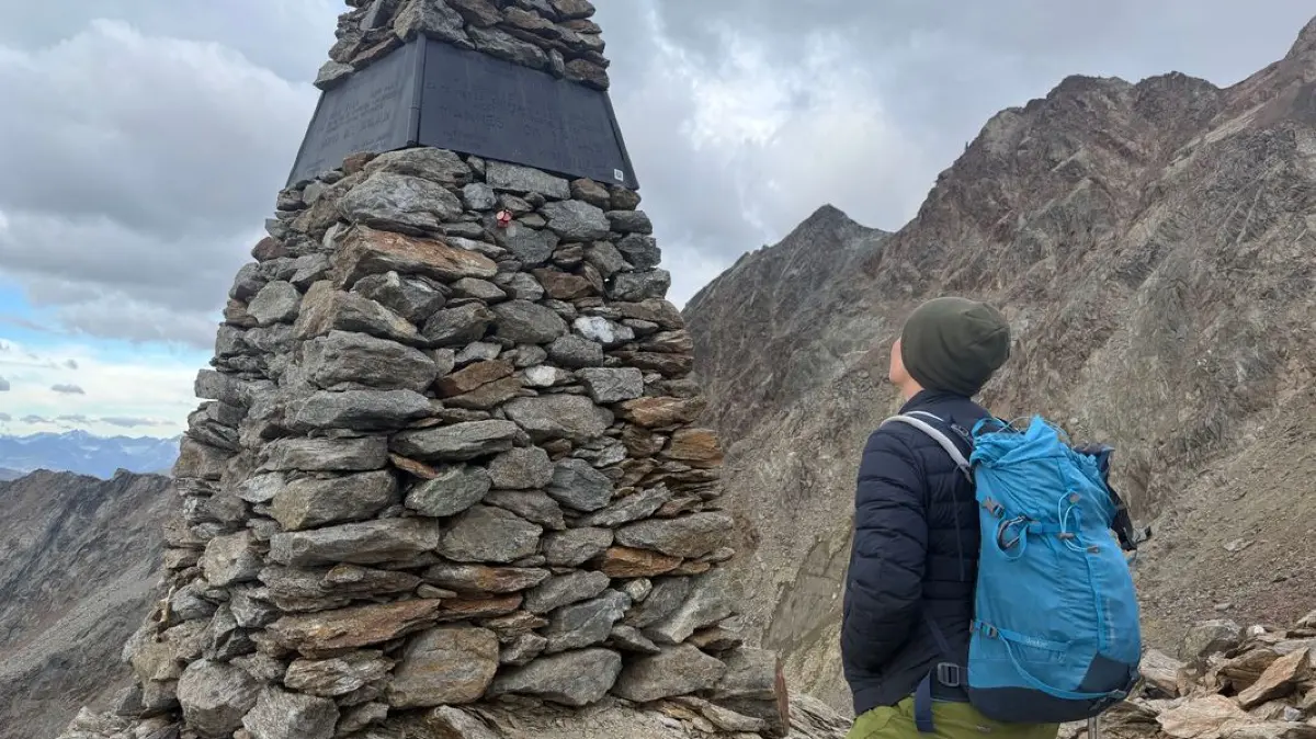 Eine Frau, die am Berg wandert, betrachtet die Gedenkstelle zum Ötzi-Fund.