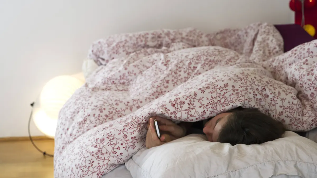 Woman lying in bed under covers, looking at smartphone PUBLICATIONxINxGERxSUIxAUTxONLY Copyright: FrédéricxCirou B30066121
