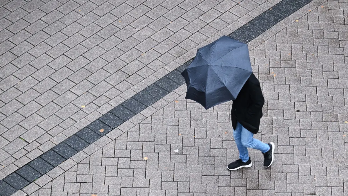 Herbstwetter in Nordrhein-Westfalen: ARCHIV - 09.10.2026, Nordrhein-Westfalen, Essen: Ein Mann geht mit seinem Regenschirm durch die Innenstadt. Die Menschen in NRW müssen am Wochenende mit herbstlichen Temperaturen, viel Wind und Regenschauern rechnen. Auch gewittern kann es am Samstag und Sonntag, wie der Deutsche Wetterdienst (DWD) mitteilt. (zu dpa: «Erst Wolken und Regen, dann bleibt es trocken in NRW») Foto: Federico Gambarini/dpa +++ dpa-Bildfunk +++