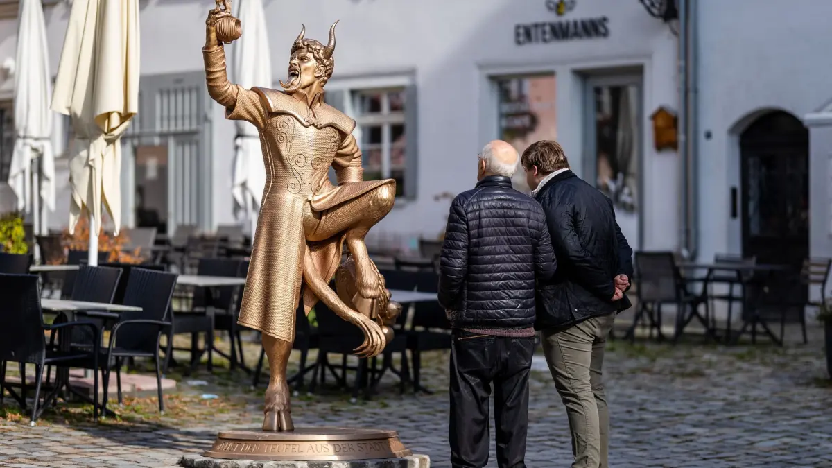 Teufelsstatue in Esslingen: Zwei Männer sehen sich die Teufelsstatue „Zwieblinger Teufel“ des Künstlers Tim Bengel an. Die Teufelsstatue sorgt in Esslingen sorgt für Ärger - Nachdem die Statue bereits beschmiert worden war, gibt es nun Morddrohungen gegen den Esslinger Oberbürgermeister Klopfer (SPD). (zu dpa: «Teufel bleibt in Esslingen - wie eine Bronze-Figur spaltet»)