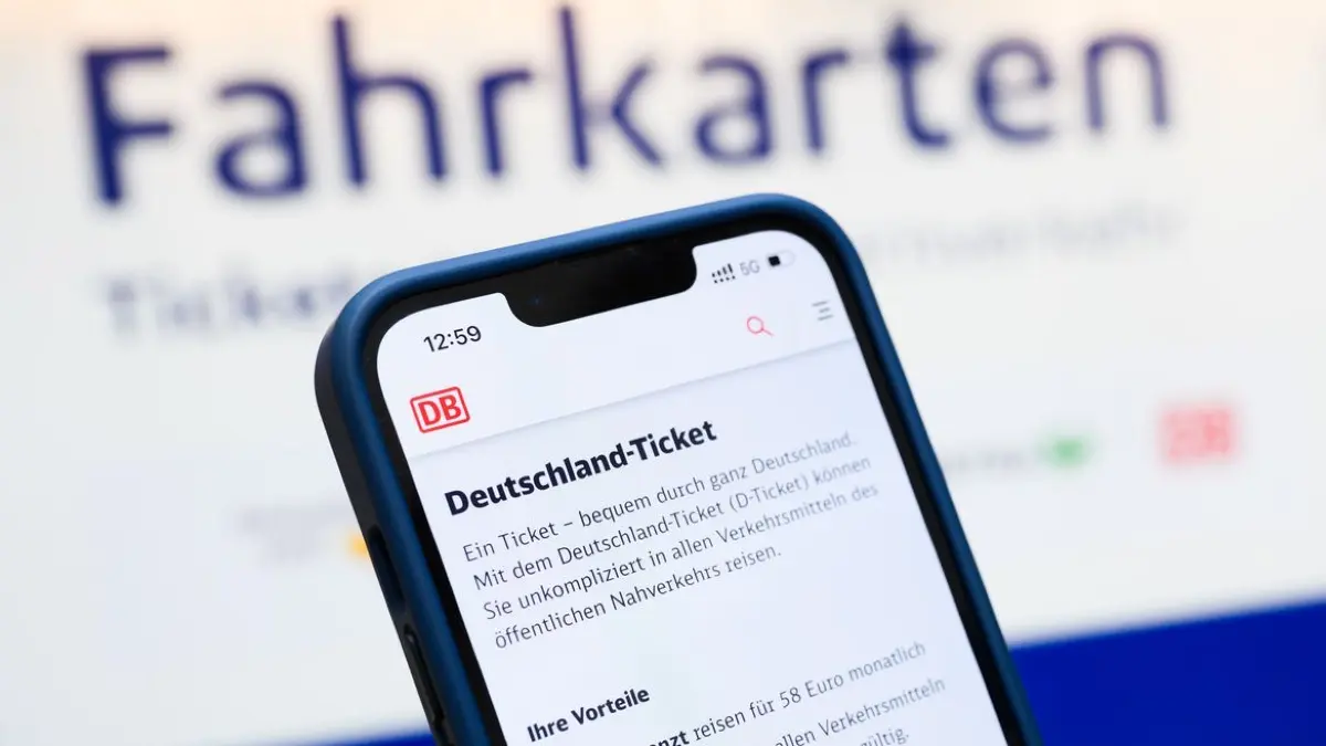 Eine Person hält ein Smartphone in der Hand, auf dessen Display eine Information zum Kauf des Deutschlandtickets zu sehen ist, während sie vor einem Fahrkartenautomaten steht.