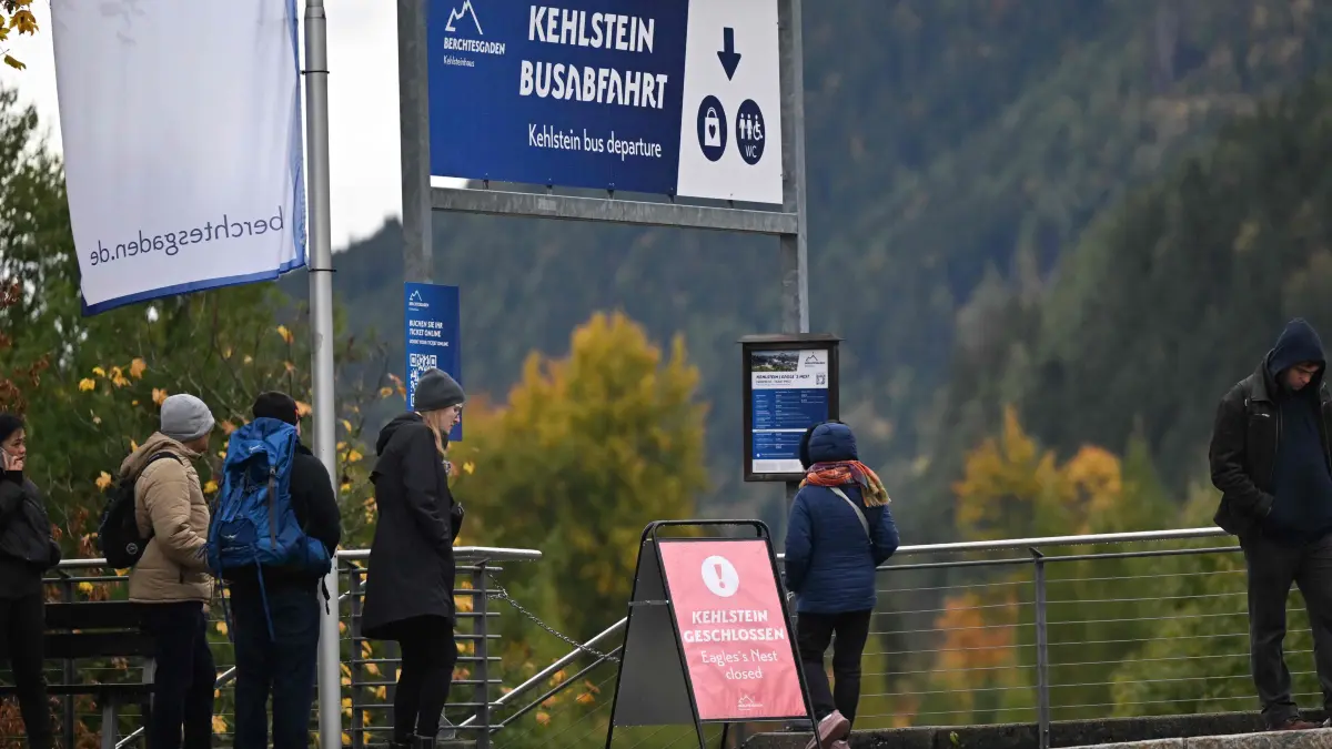 GERMANY-HISTORY-POLICE-FIRE-HITLER: People stand at the bus departure for the bus going to the mountain guesthouse Kehlsteinhaus, known as the Eagle's Nest, formerly Adolf Hitler's mountain retreat, on October 24, 2026, as a sign reads "Kehlstein house closed" after a large fire had broken out at the site located at an altitude of 1,834 metres (6,000 feet) in the mountains over Berchtesgaden, in the southern German state of Bavaria. Emergency services arrived on site on late October 23, 2026 and found a large fire. German police said on October 24, 2026 they have detained a suspect following a fire at Adolf Hitler's mountain retreat, known as the Eagle's Nest. (Photo by KERSTIN JOENSSON / AFP)
