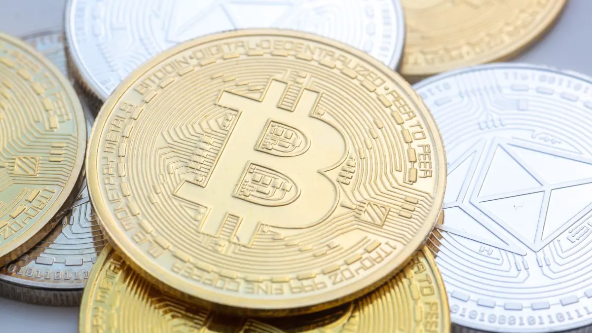Kryptowährung: Münzen mit den Symbolen von Bitcoin (M) und Ethereum sind auf einem Tisch angeordnet. (zu dpa: «Milliardenschwerer Hackerangriff auf Kryptobörse Binance»)
